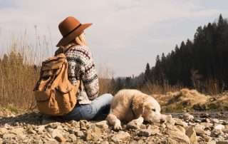 women sitting on top of mountain gazing out with golden retriever laying beside her.